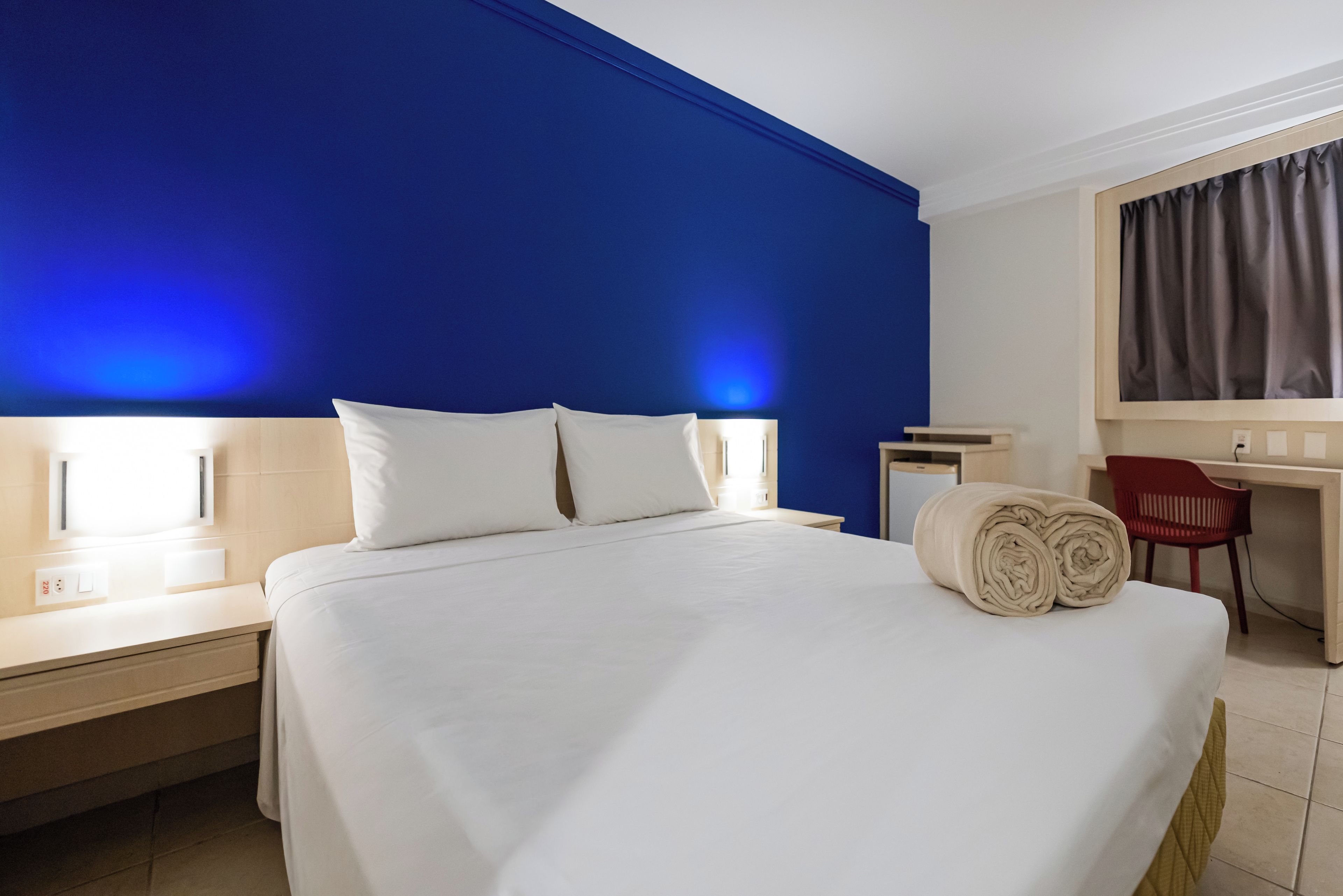 Quarto de hotel com uma cama grande, uma escrivaninha e uma cadeira.