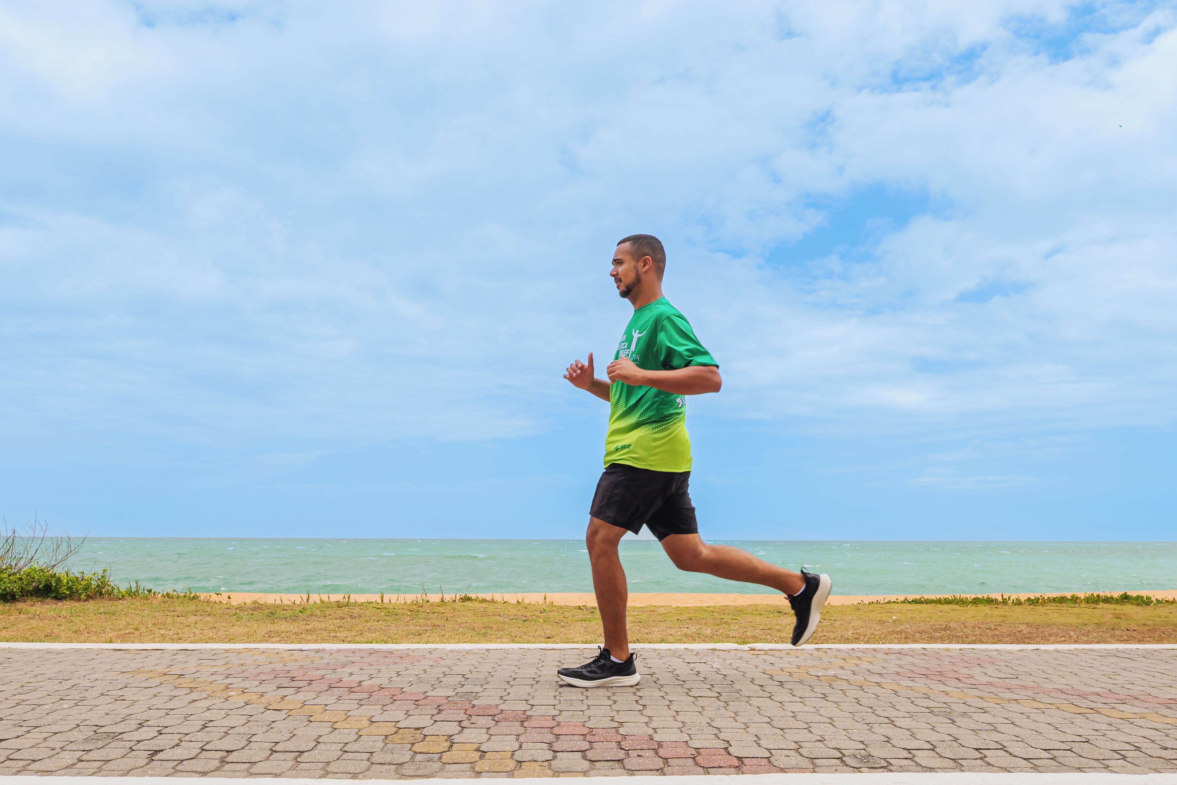 A person jogging on a paved path with a beach and ocean in the background.