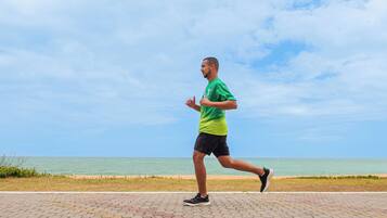 A person jogging on a paved path with a beach and ocean in the background.