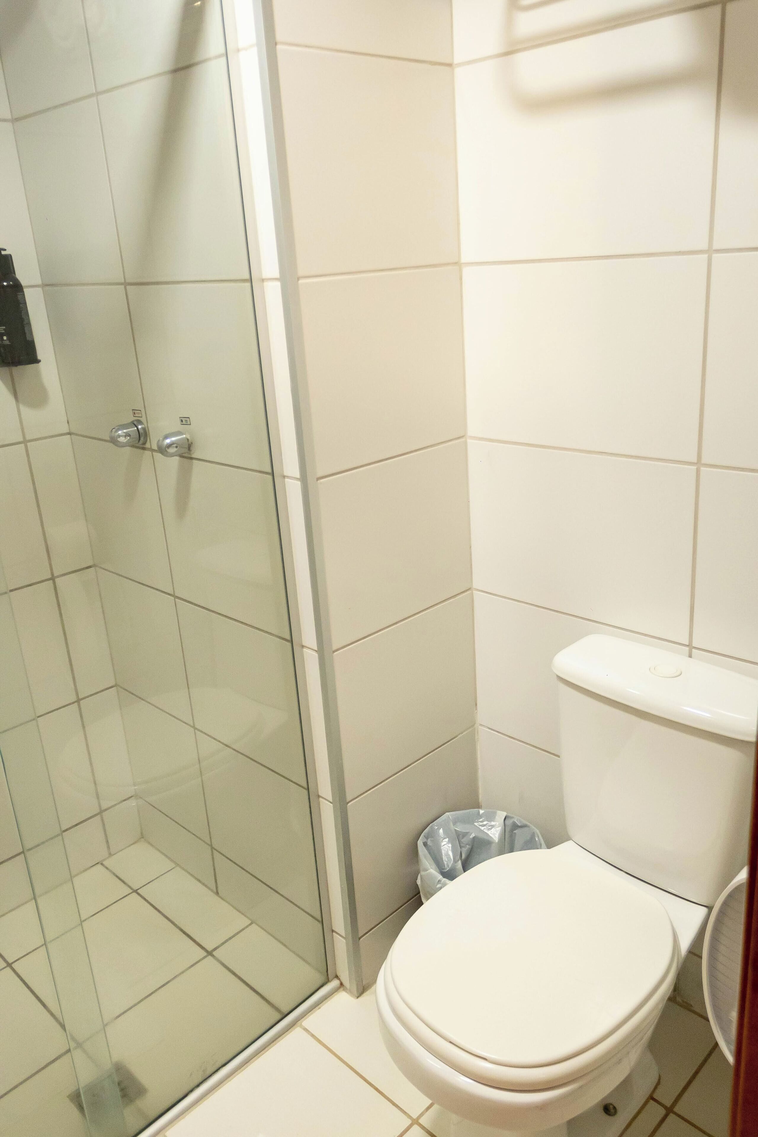 A bathroom with a glass shower enclosure, a toilet, and a trash bin.