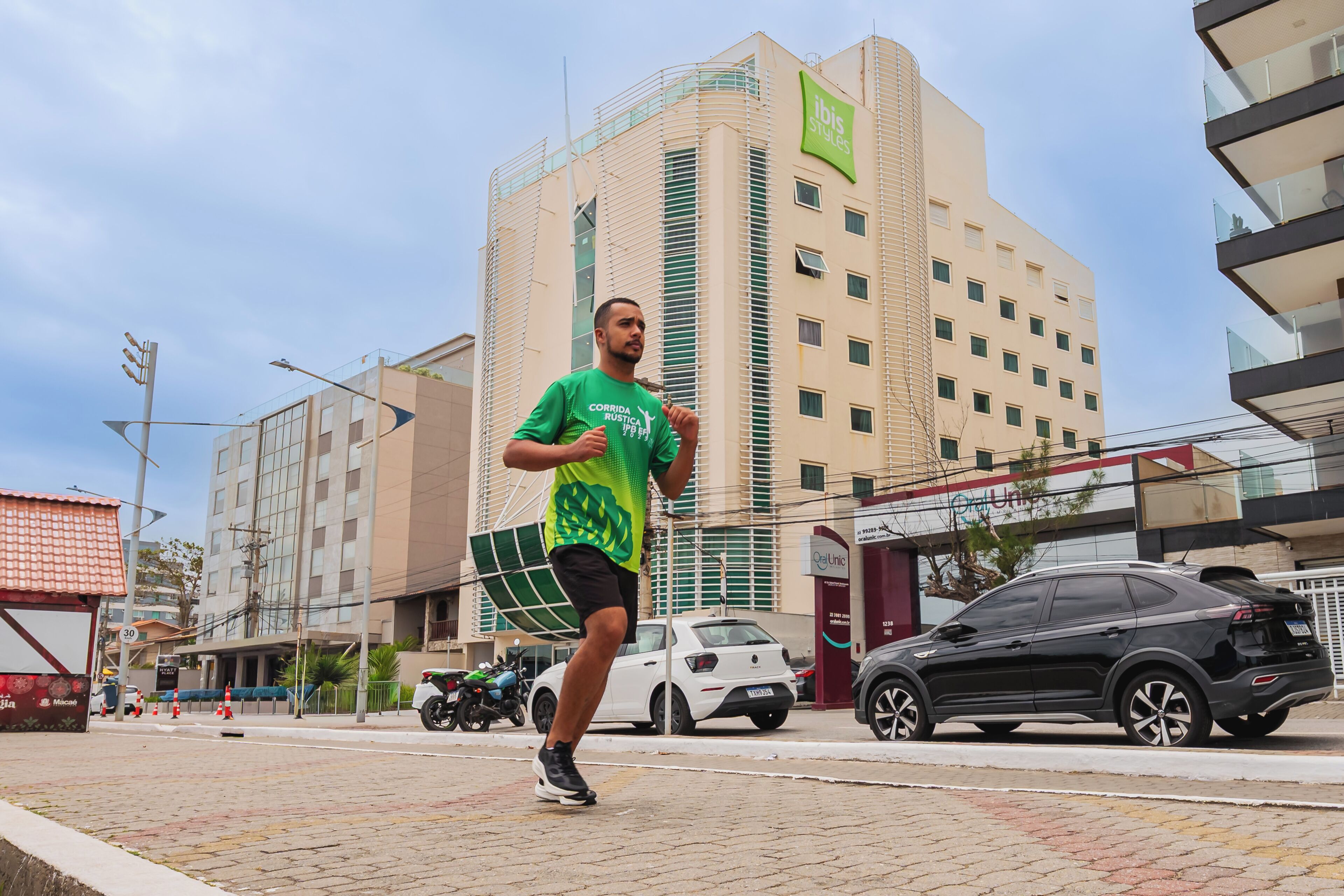 A man running on a paved area with buildings in the background, including a hotel with a sign that reads 'ibis suites'.