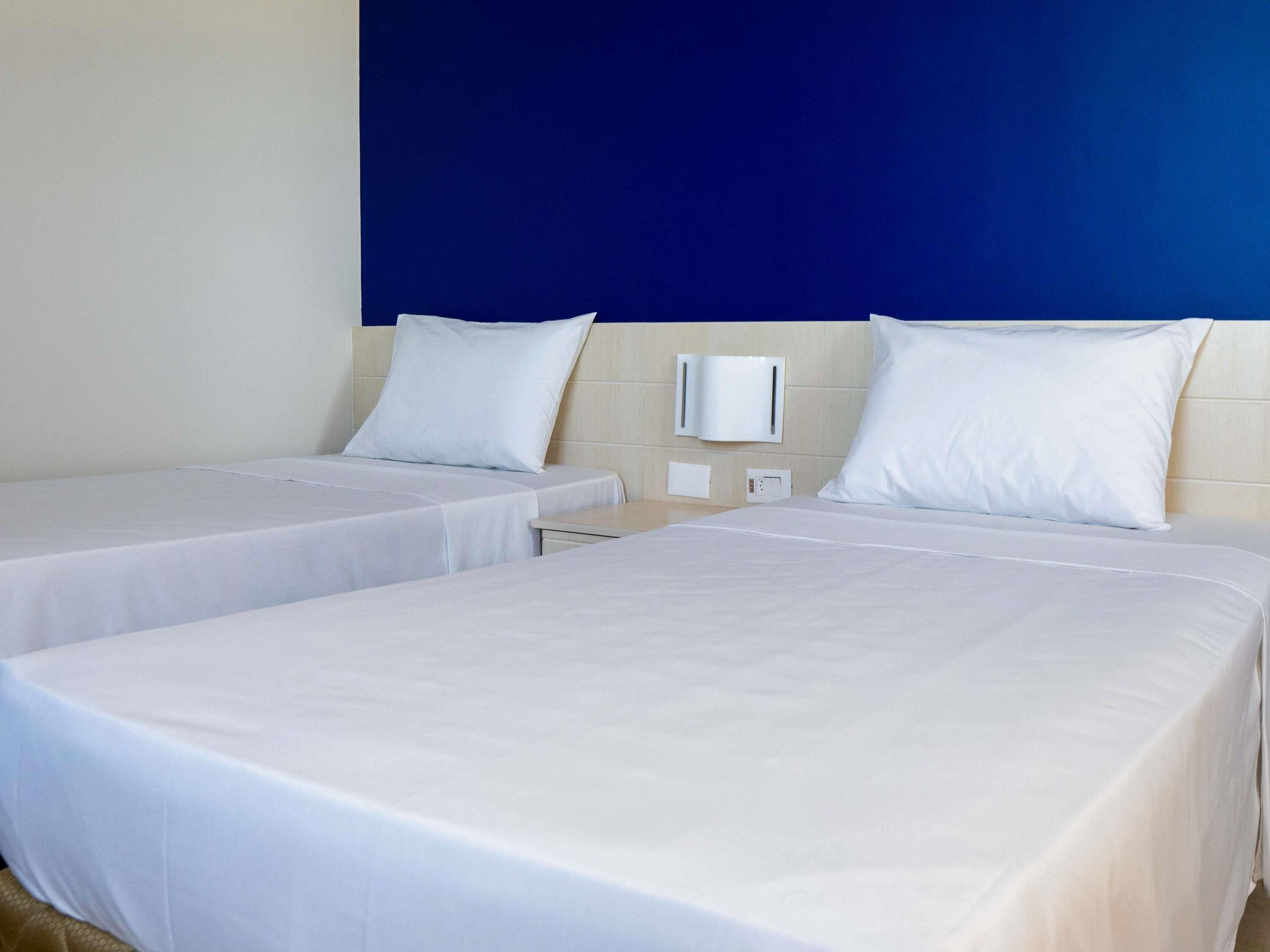 Une chambre d’hôtel avec deux lits simples, un mur d’accent bleu et une table de chevet blanche avec une lampe.