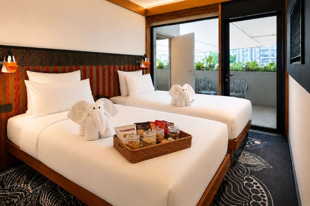 A hotel room with two beds, a wicker tray with snacks, and a view of the city.