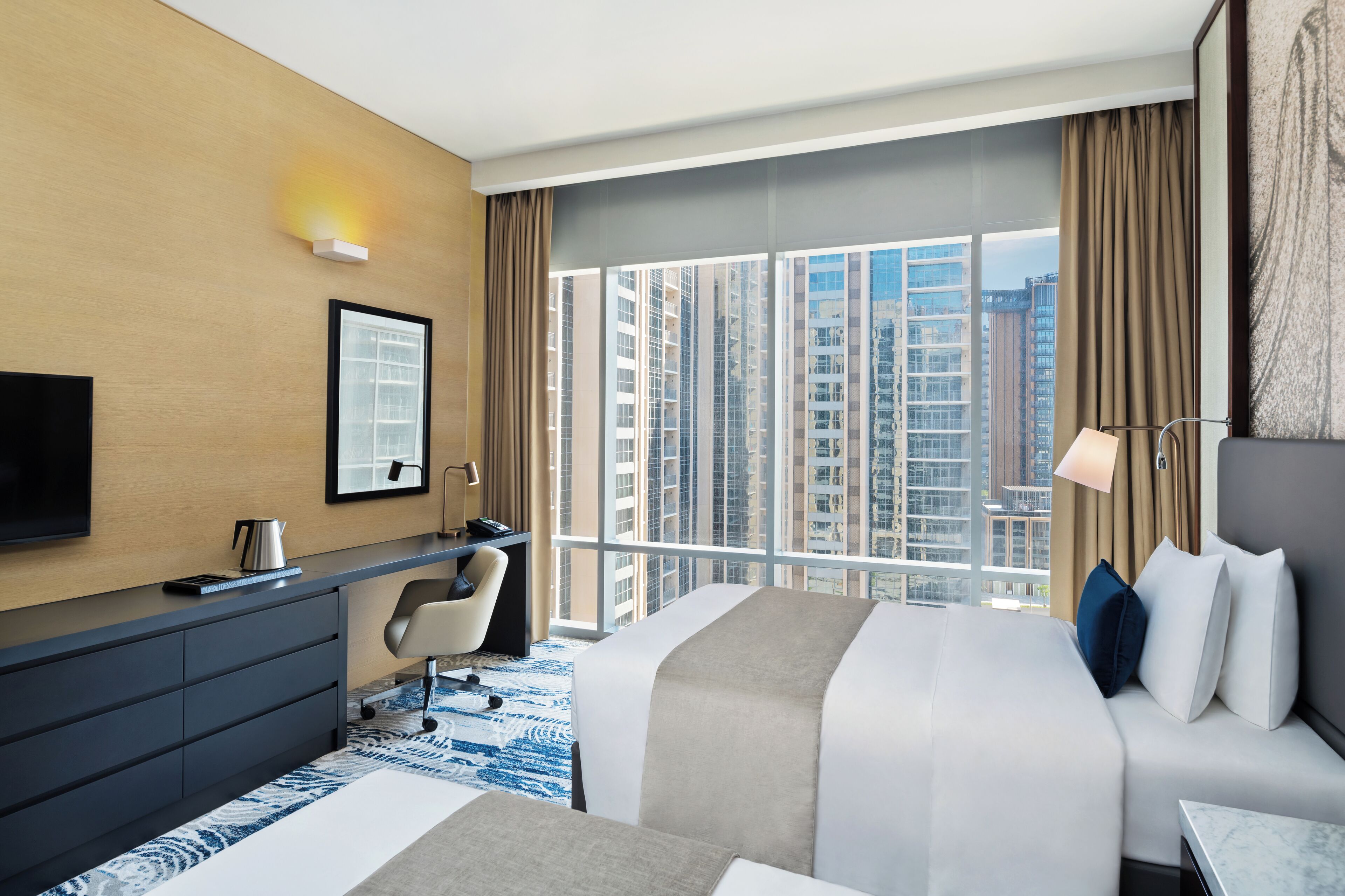 Een moderne hotelkamer met een groot bed, een bureau, een flatscreen-tv en stadszicht door grote ramen.