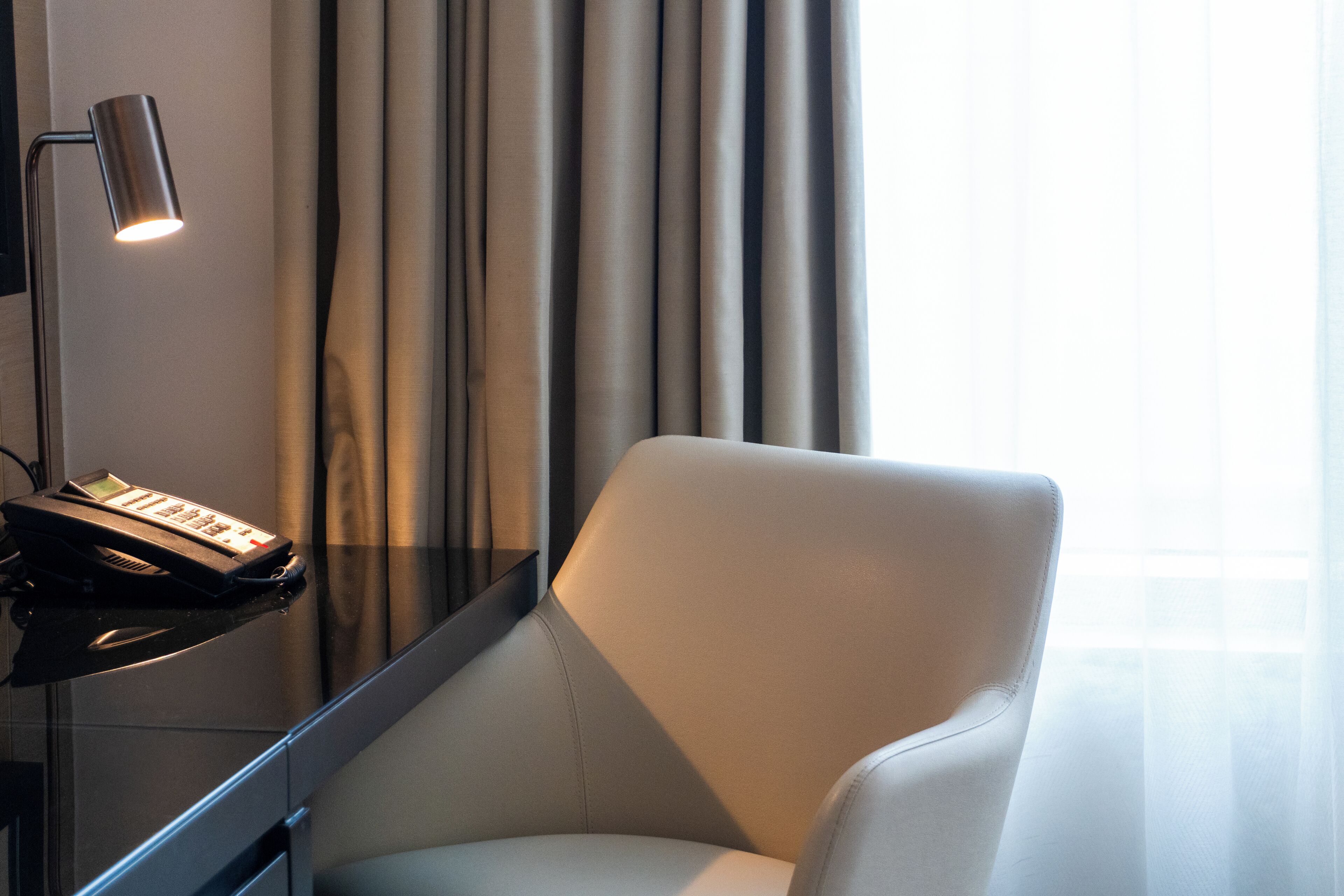 A modern room with a leather armchair, a desk with a lamp, and a window with curtains.