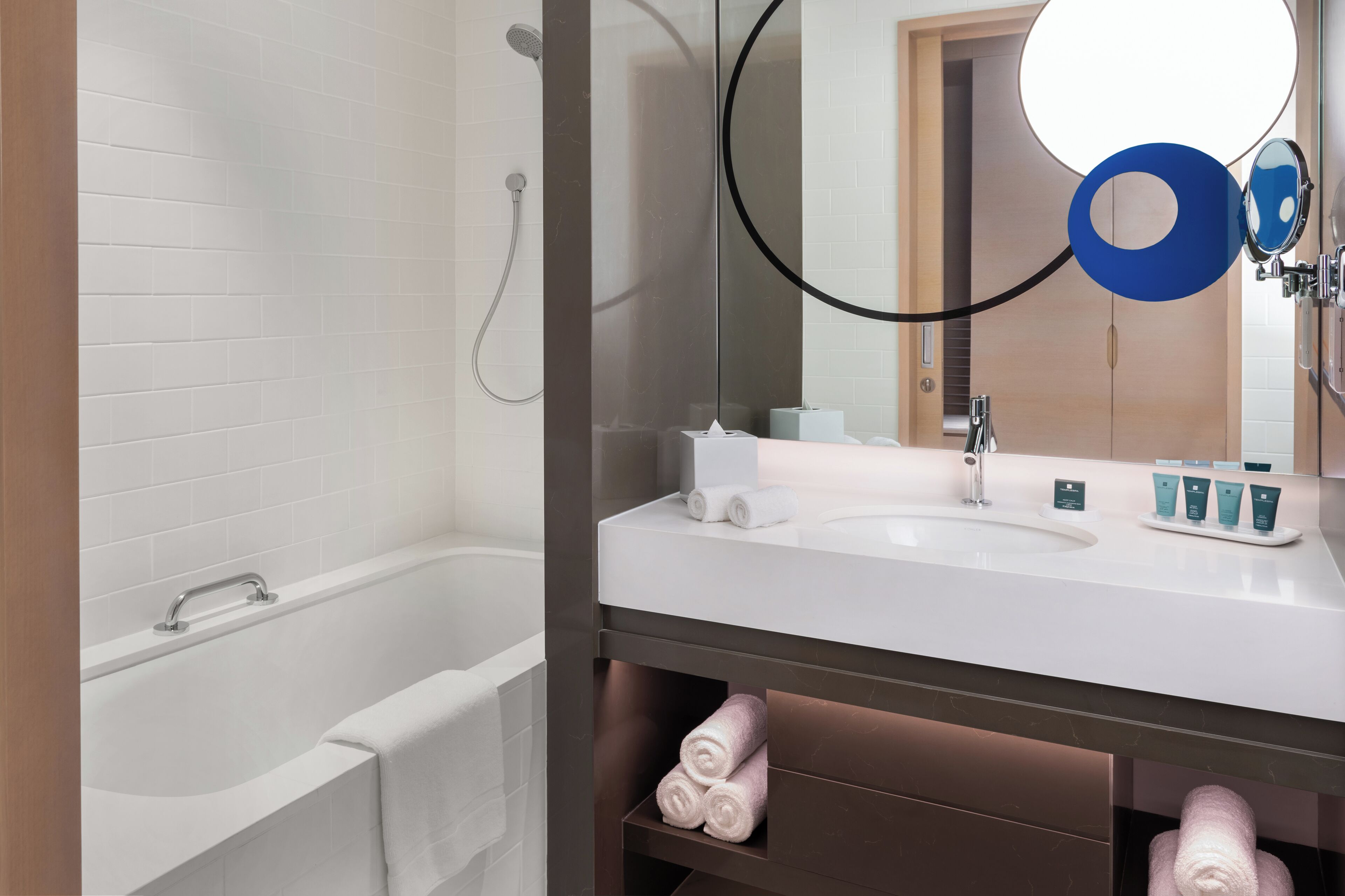 Une salle de bain moderne avec une baignoire blanche, un grand miroir et un meuble-lavabo avec des articles de toilette.
