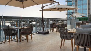 Um terraço no telhado com área de estar externa, vista da cidade e um prédio alto ao fundo.