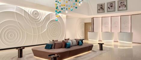 A modern lobby with a curved sofa, a decorative hanging light fixture, and a reception desk.