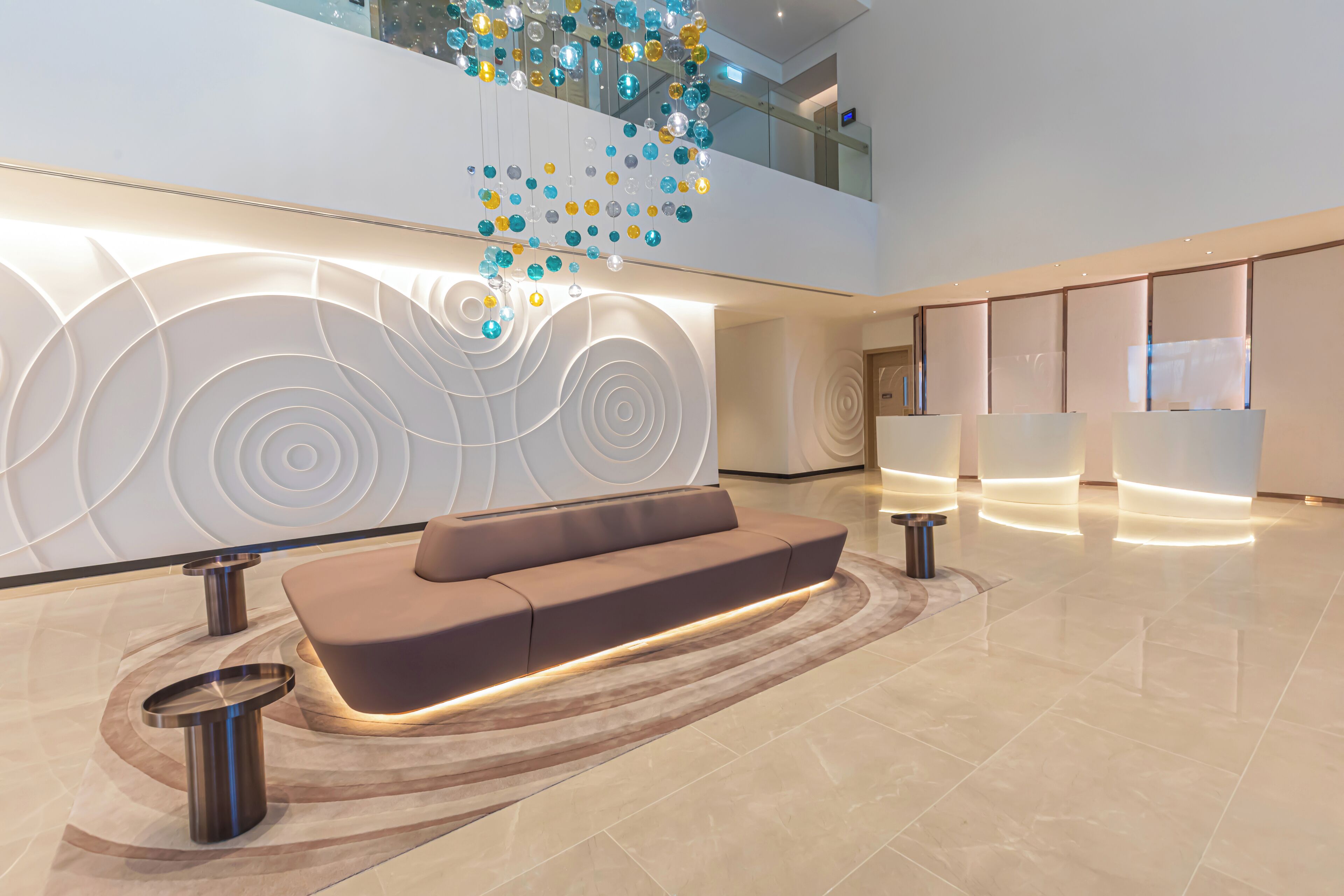 A modern lobby with a central seating area, a decorative light installation, and a reception desk.