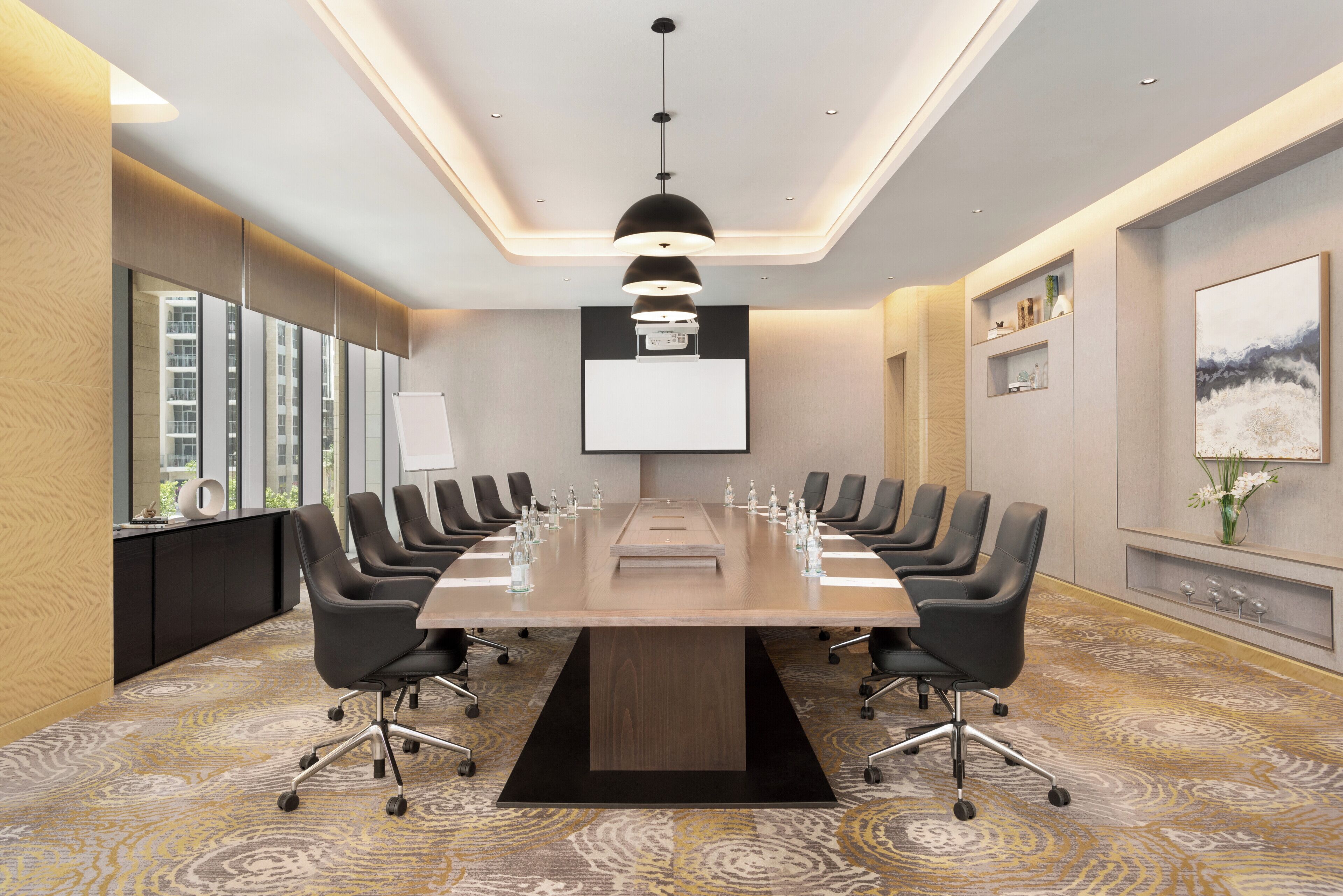 A conference room with a long table, chairs, a projector screen, and a large window.