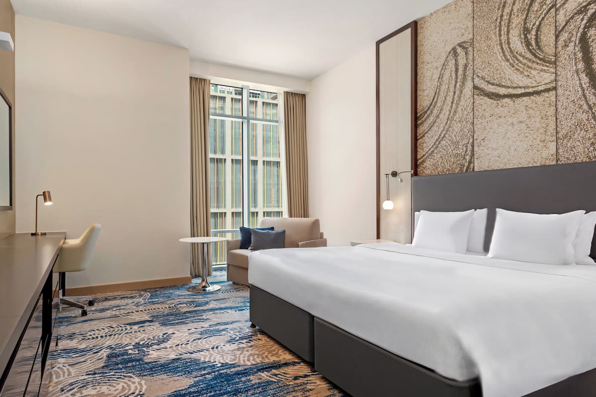 Une chambre d’hôtel avec un grand lit, un bureau, une chaise, une petite table et une fenêtre avec des rideaux.