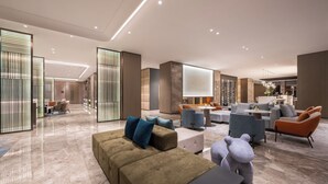 Un hall d’entrée spacieux au design moderne, comprenant un espace salon avec des canapés et des fauteuils, un coin repas et un comptoir d’accueil.