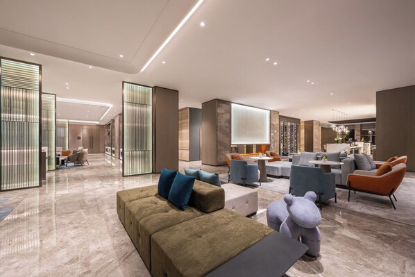 A spacious lobby with a modern design, featuring a seating area with sofas and armchairs, a dining area, and a reception desk.