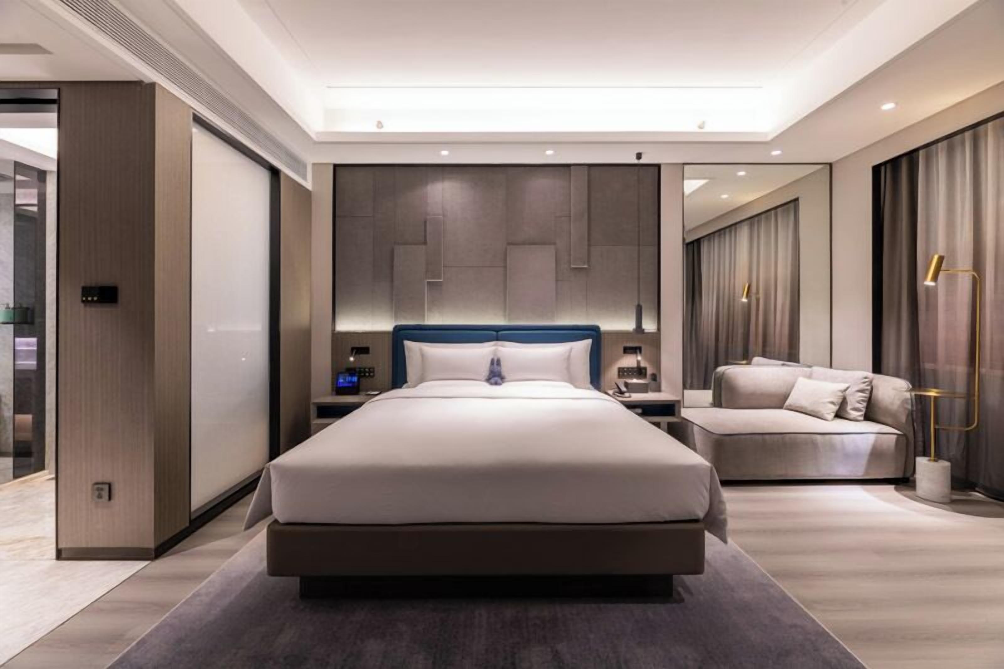 Une chambre d’hôtel moderne avec un grand lit, un canapé, une table de chevet et un miroir.
