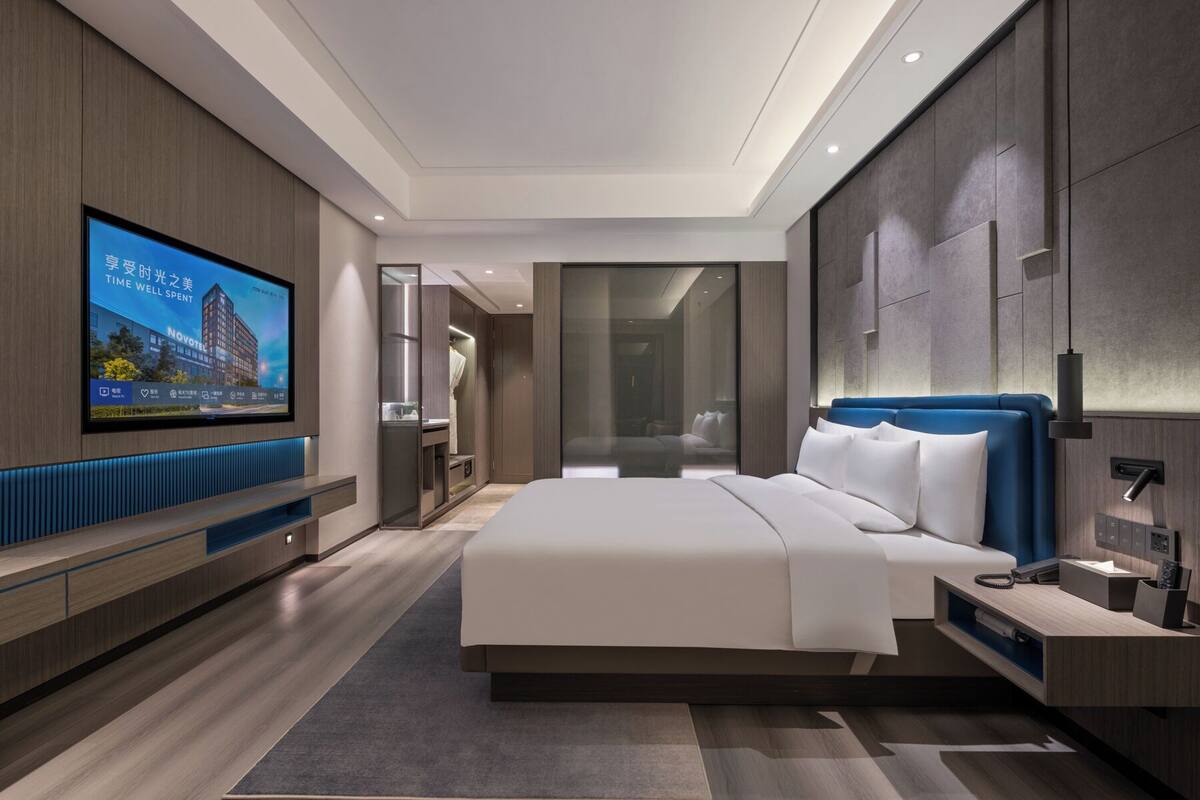 A modern hotel room with a large bed, a TV on the wall, and a walk-in closet.
