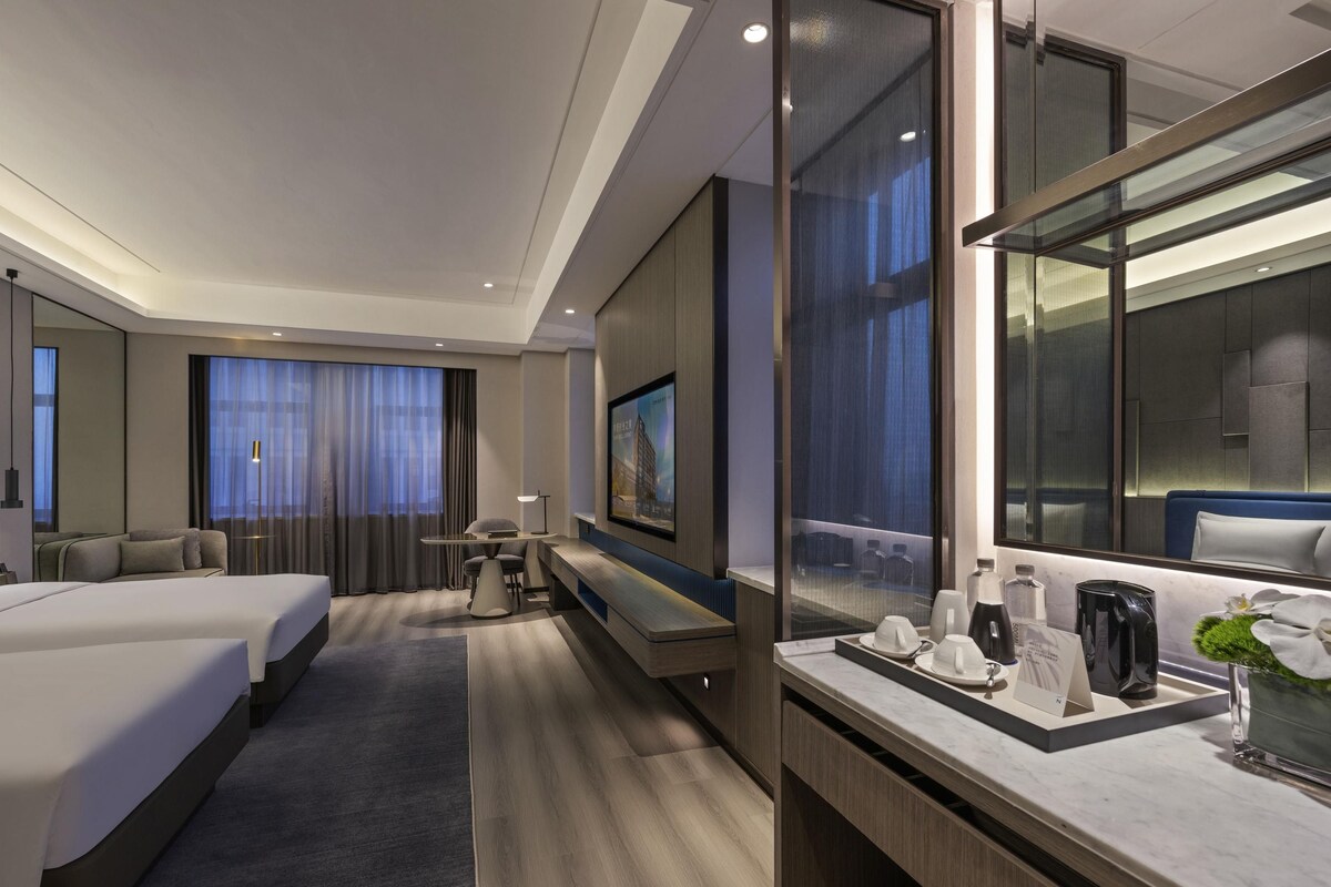 Een hotelkamer met een bed, een bureau, een stoel, een televisie en een spiegel in de badkamer.