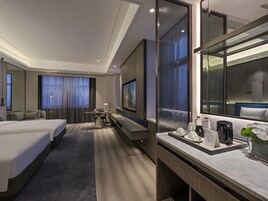 Habitación de hotel con cama, escritorio, silla, televisor y espejo de baño.