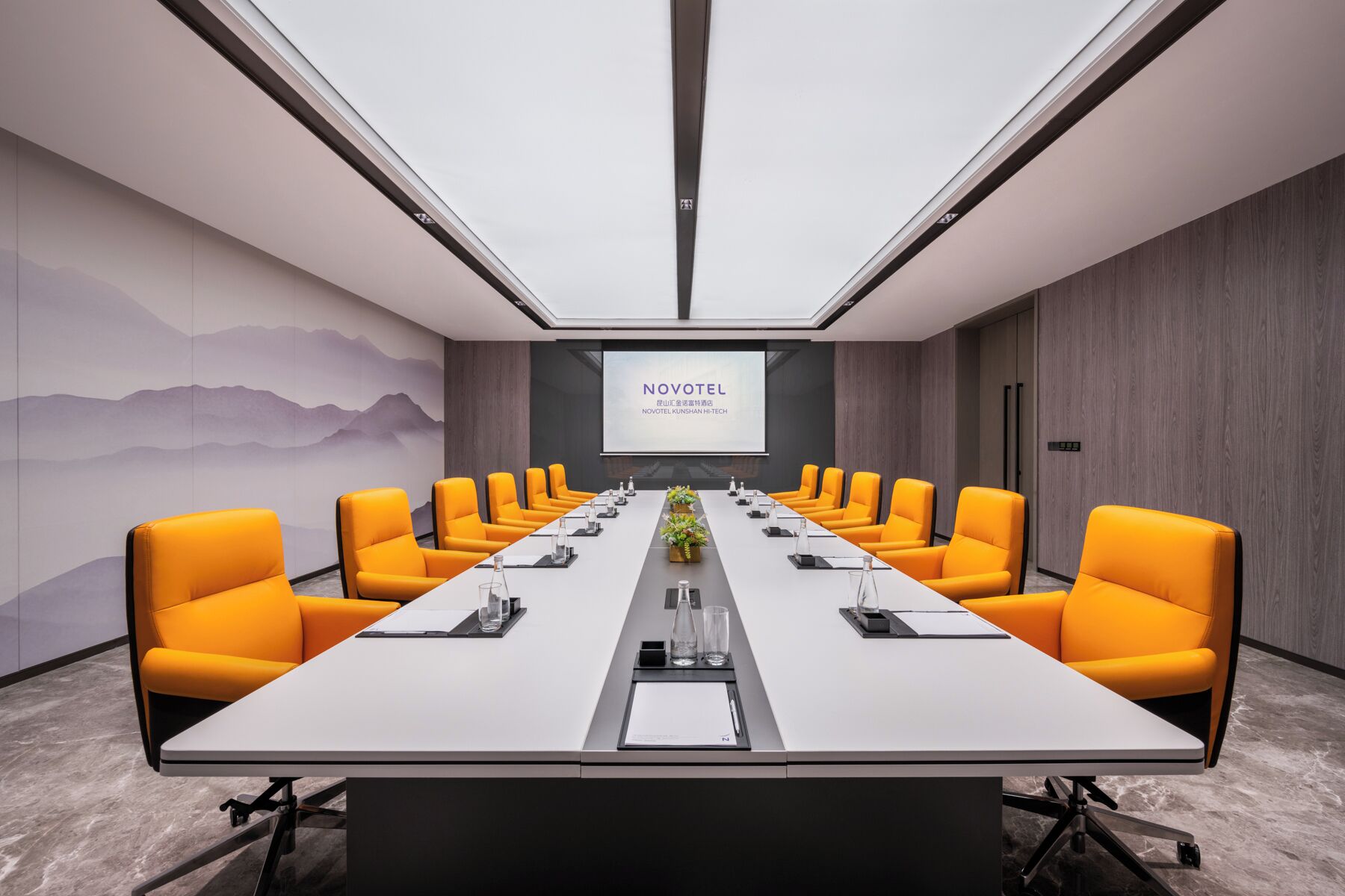 A conference room with a long table, multiple chairs, a projector screen, and a decorative wall.