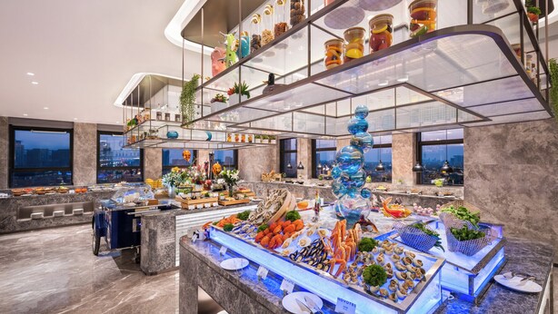 Un hall d’hôtel moderne avec un buffet de fruits de mer, un escalier en verre et une vue sur la ville.