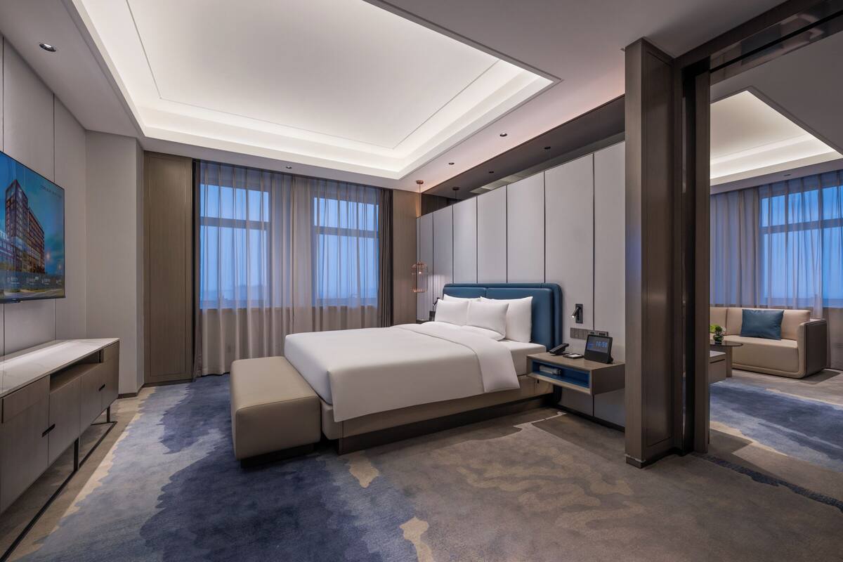 A modern hotel room with a large bed, a desk, and a seating area.