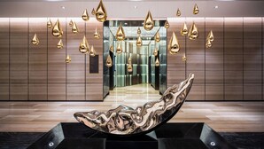 Un hall d’entrée moderne agrémenté d’une sculpture réfléchissante, d’un mur miroir et d’un espace ascenseur au design épuré.
