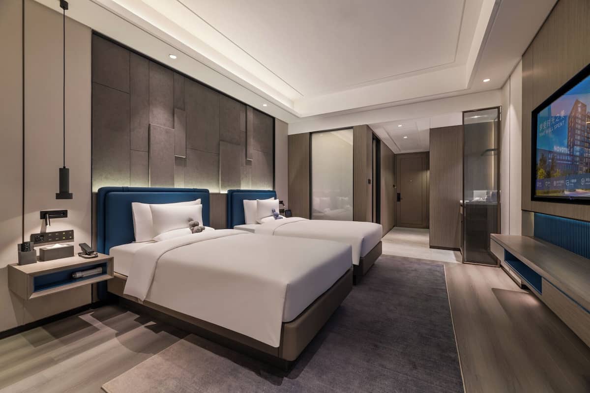 A modern hotel room with two beds, a TV, and a minibar.