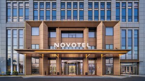 Une entrée d'hôtel moderne, avec une enseigne « NOVOTEL » bien visible, de grandes portes vitrées et une façade symétrique.