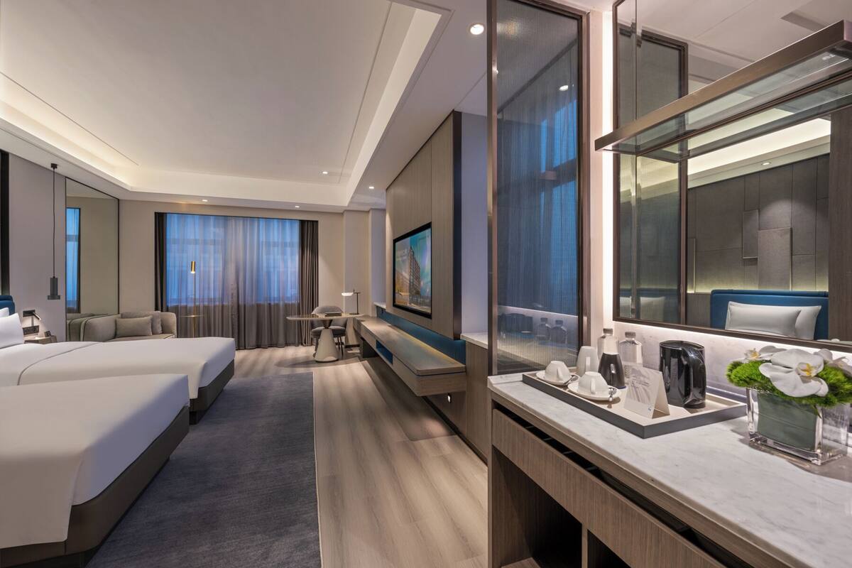 A modern hotel room with a large bed, a desk, a seating area, and a large mirror.