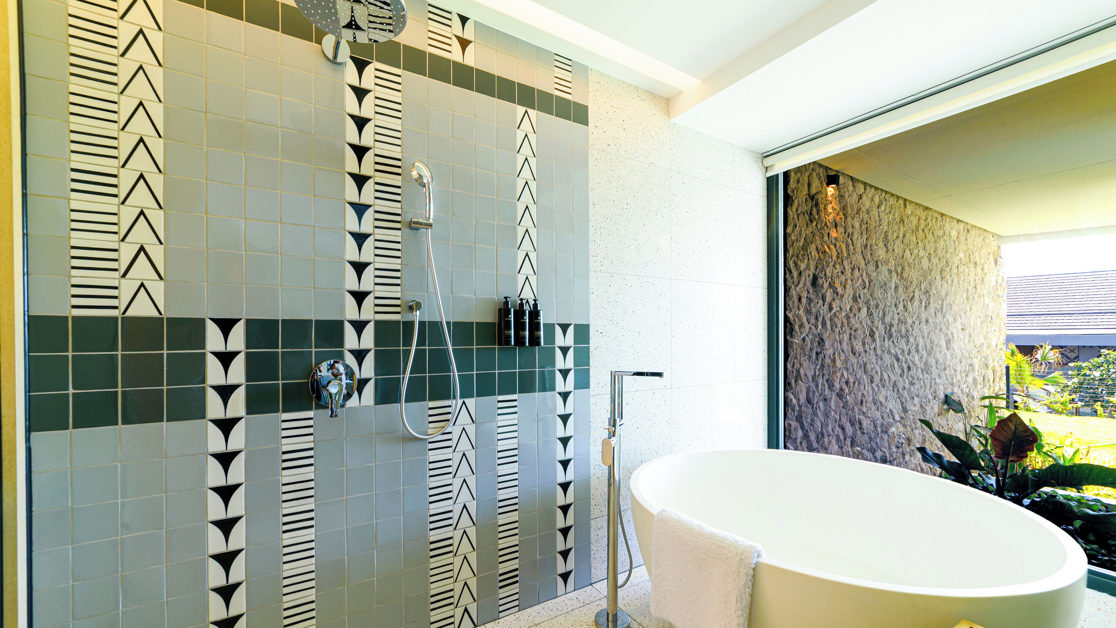 Une salle de bain dotée d’une baignoire sur pieds, d’une douche avec un robinet mural et d’un mur recouvert de carreaux aux motifs géométriques.
