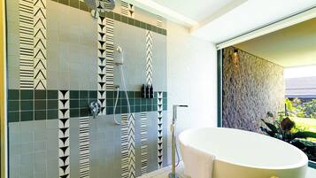 Une salle de bain dotée d’une baignoire sur pieds, d’une douche avec un robinet mural et d’un mur recouvert de carreaux aux motifs géométriques.