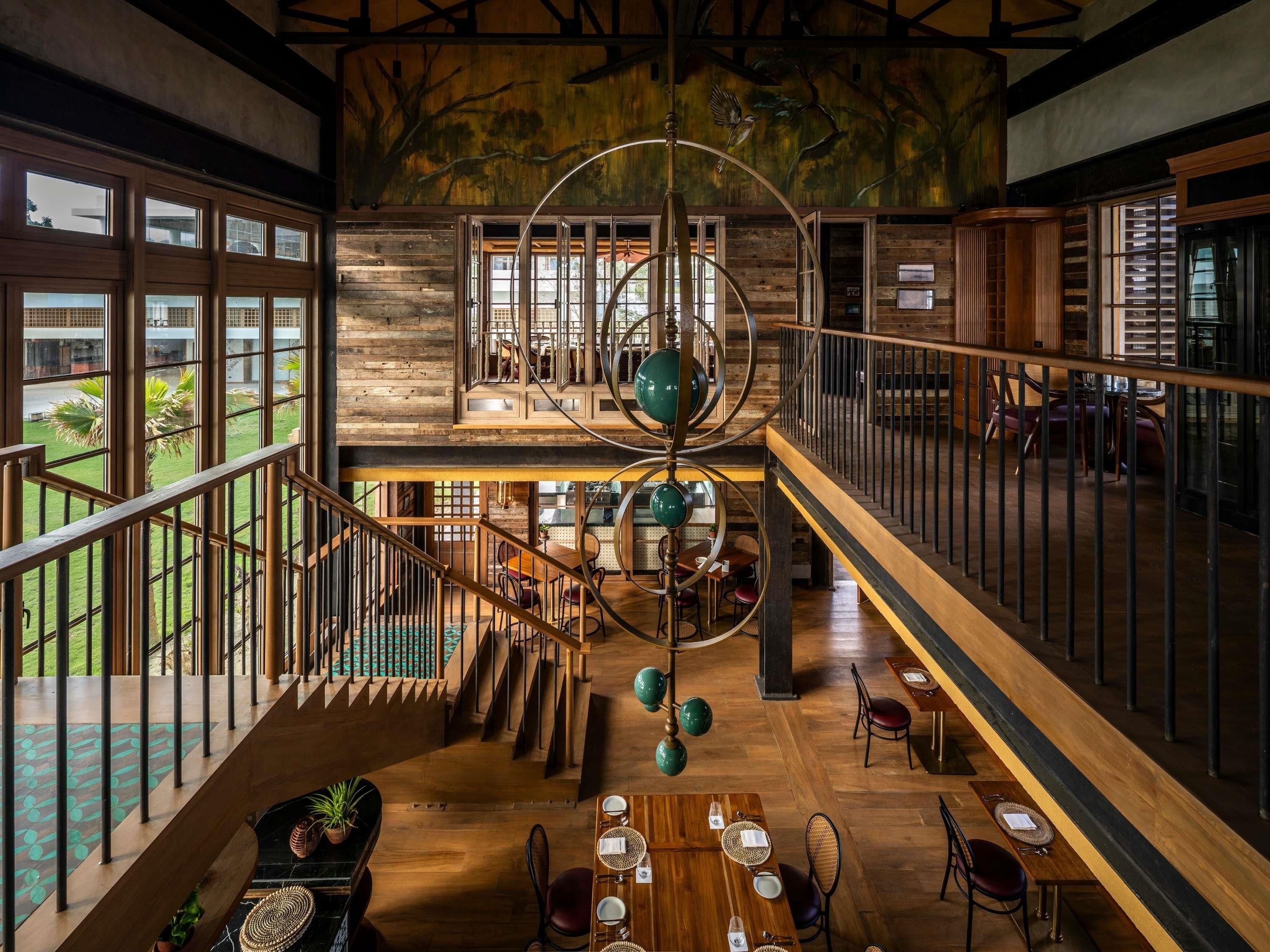 A spacious interior with a central staircase, wooden flooring, and a dining area with tables and chairs.