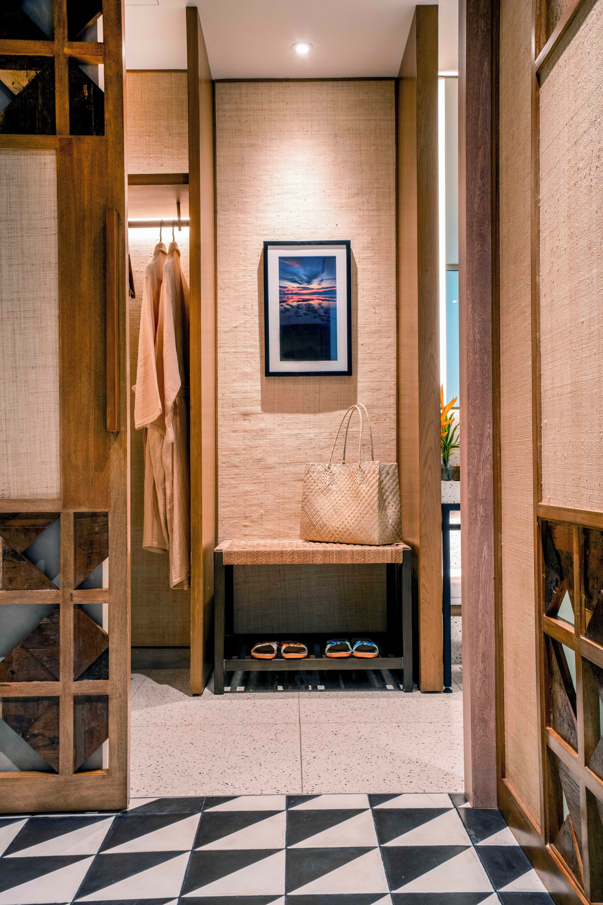 A hallway with a wooden bench, a hanging coat rack, and a framed picture on the wall.