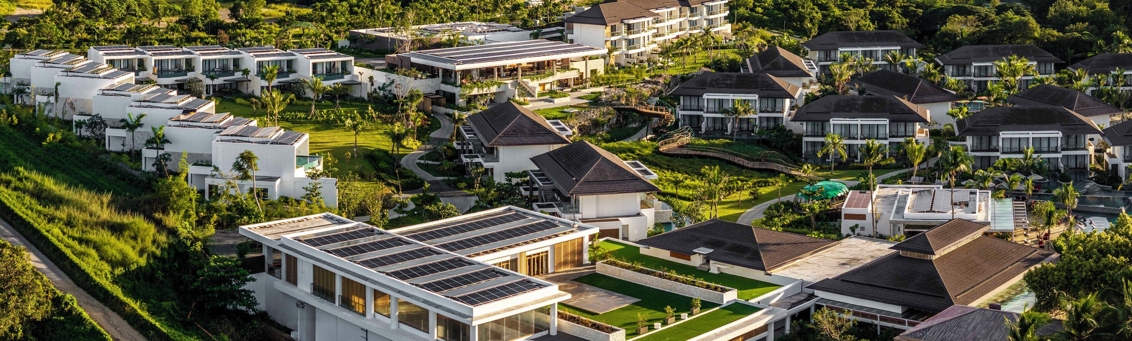 A modern resort with multiple buildings, solar panels, and lush greenery.