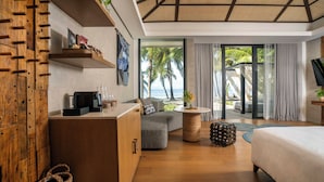 A modern hotel room with a wooden cabinet, a sofa, a bed, a round coffee table, and a view of the beach. - South Palms Resort And Spa Panglao - Mgallery Collection (Panglao)