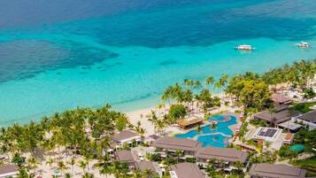 Un resort con varias edificaciones, una piscina y una playa de aguas turquesas cristalinas.