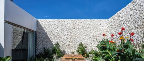 An outdoor dining area with a stone wall, wooden table, wicker chairs, and potted plants.