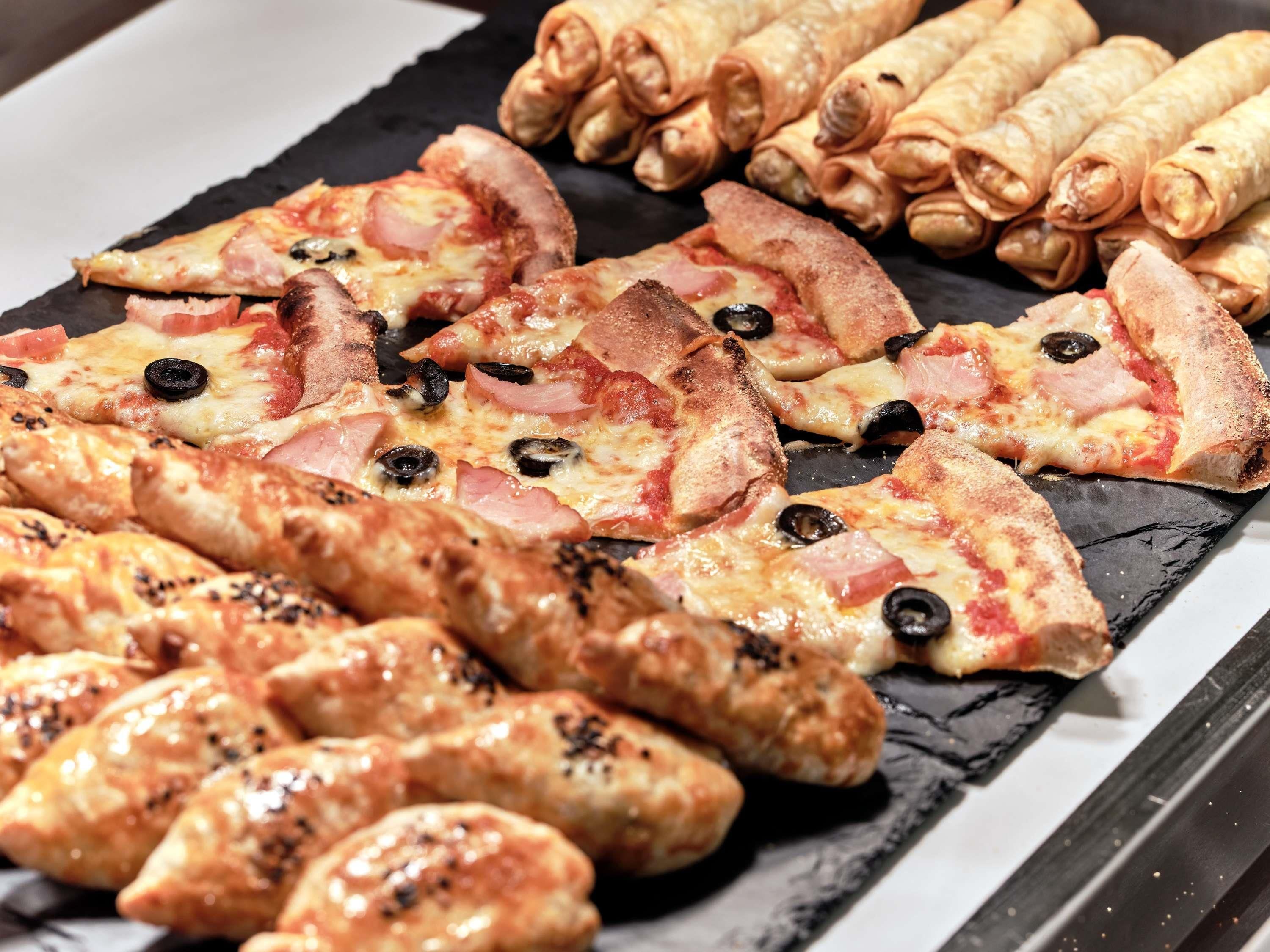 Variedad de alimentos como pizza, panecillos y pasteles en una tabla de pizarra.