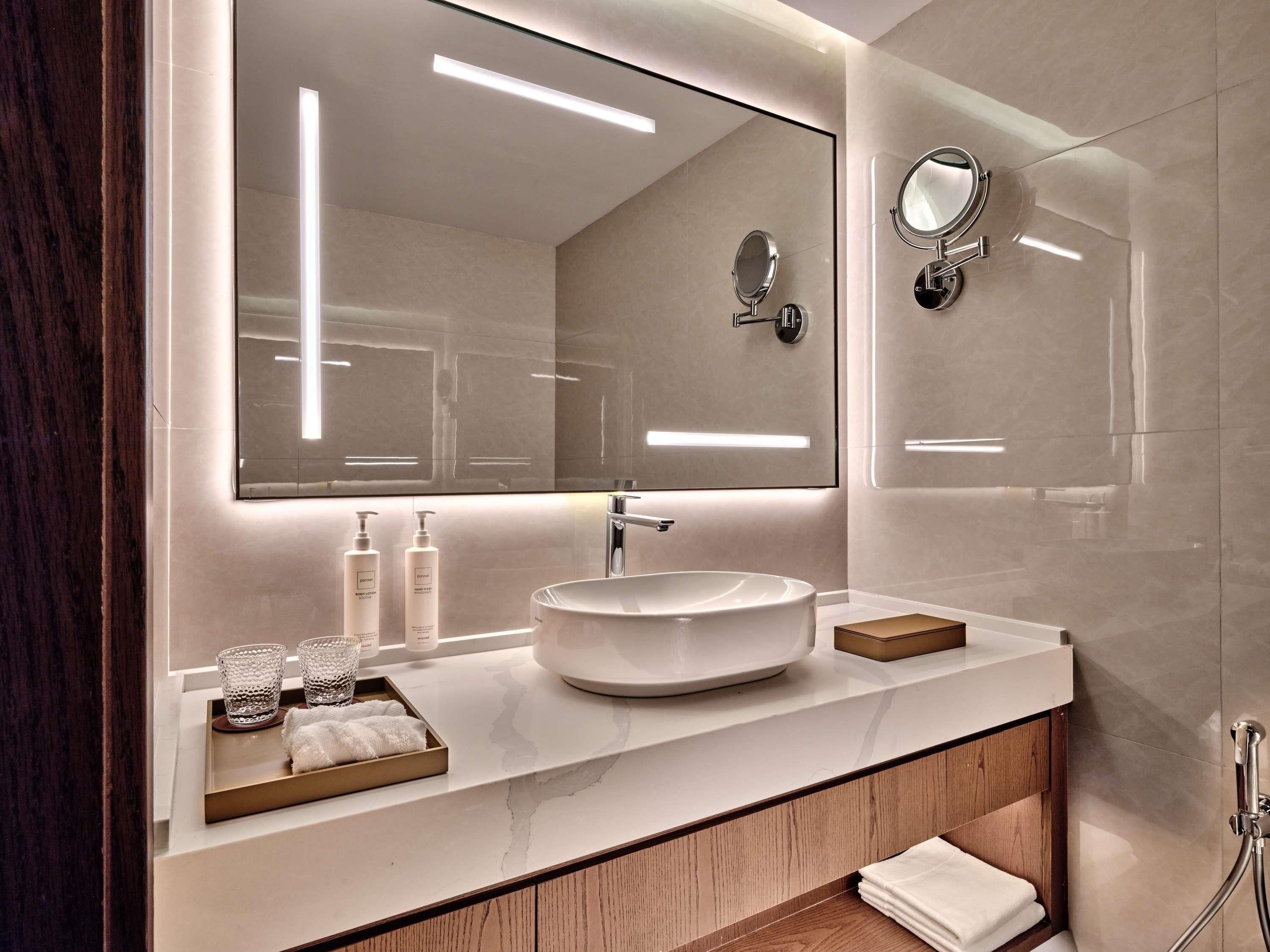 Une salle de bain moderne avec un grand miroir, un lavabo rond et un meuble-lavabo sur lequel est posé un plateau contenant des articles de toilette.