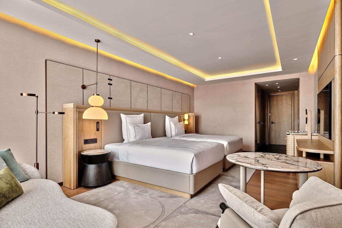 A modern hotel room with a large bed, a round coffee table, and a seating area with two chairs.