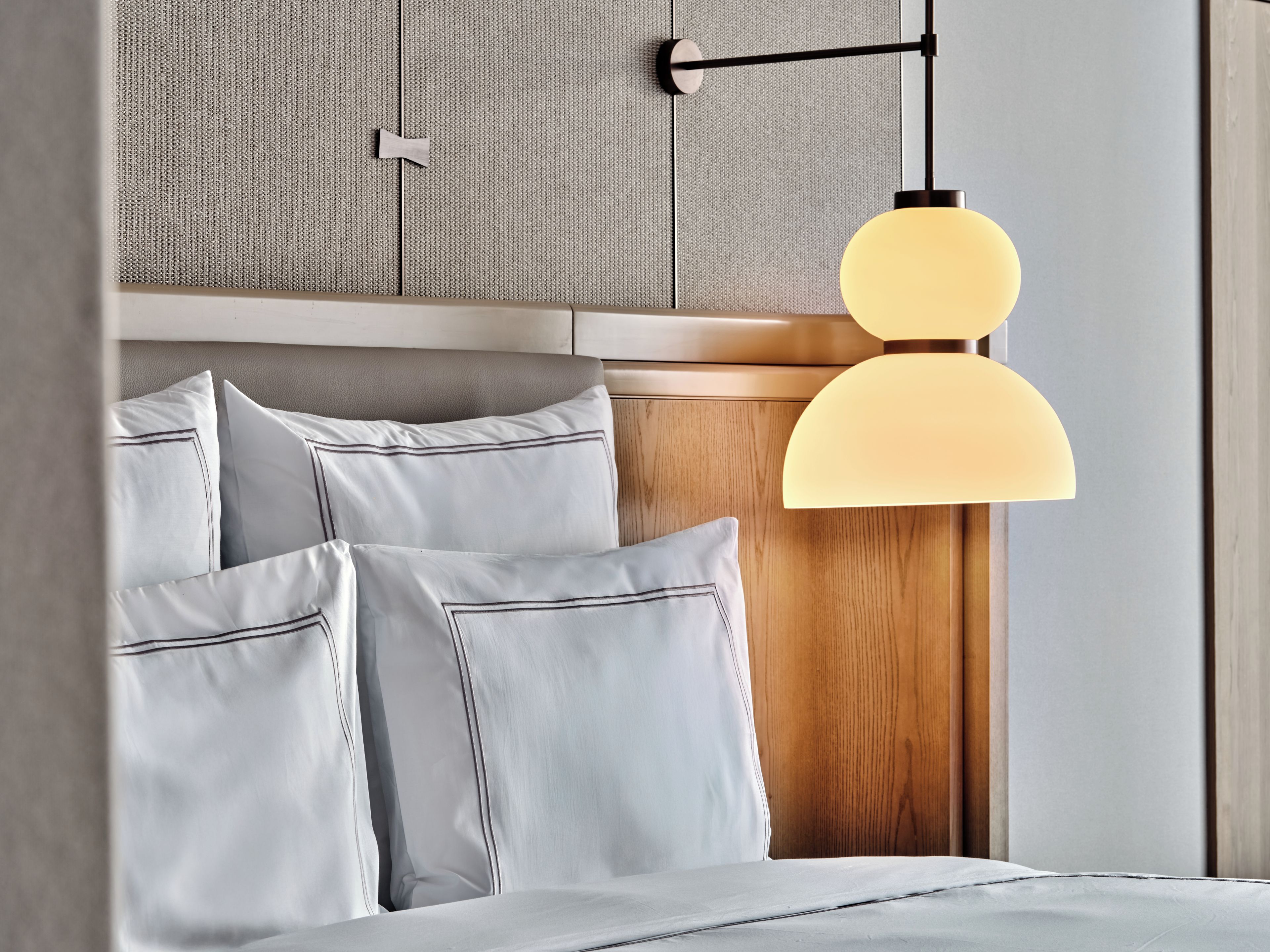 A bed with pillows and a hanging pendant light fixture.