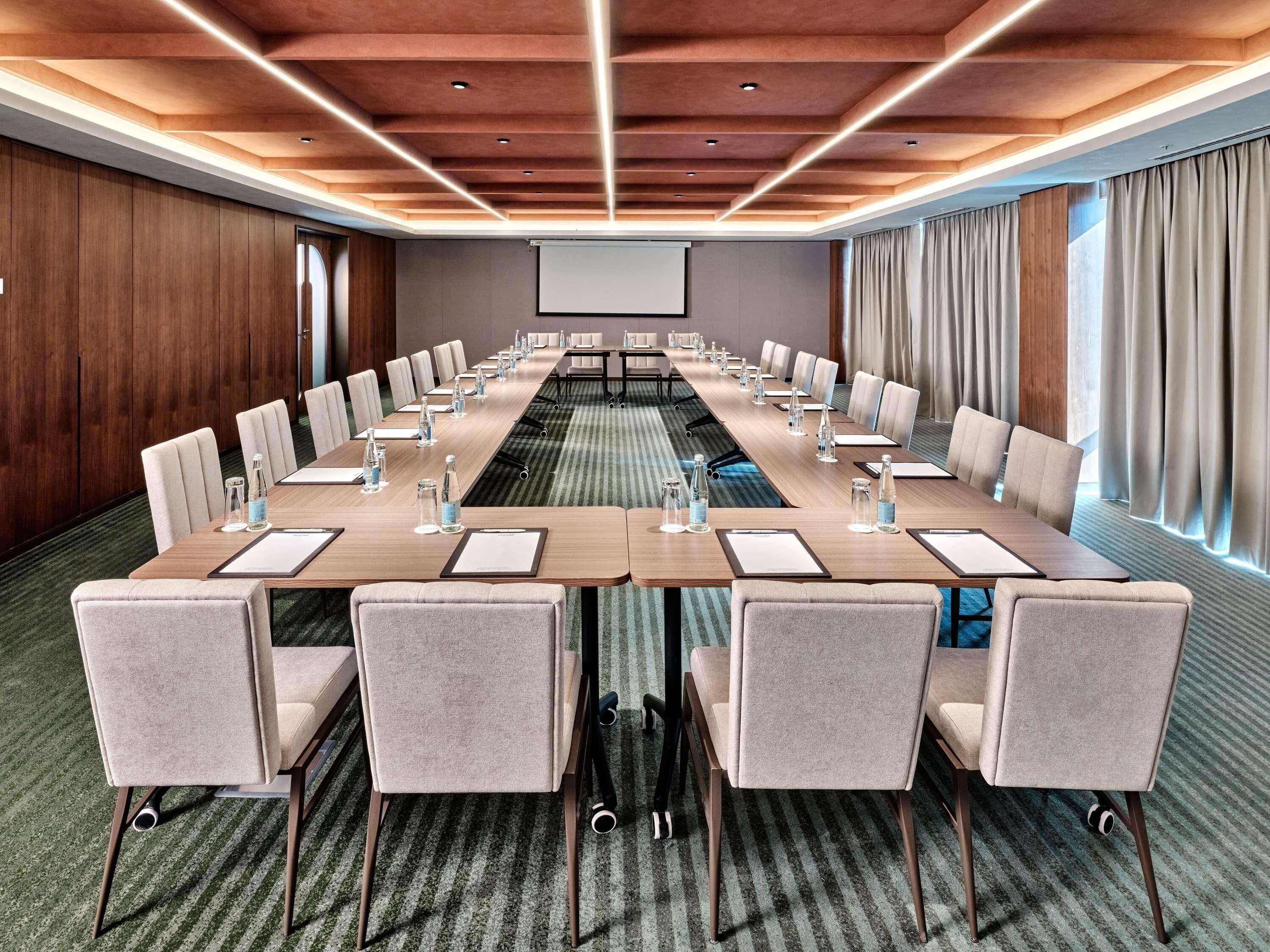 A conference room with a long table, chairs, water bottles, and a projector screen.