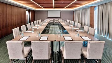 A conference room with a long table, chairs, water bottles, and a projector screen.