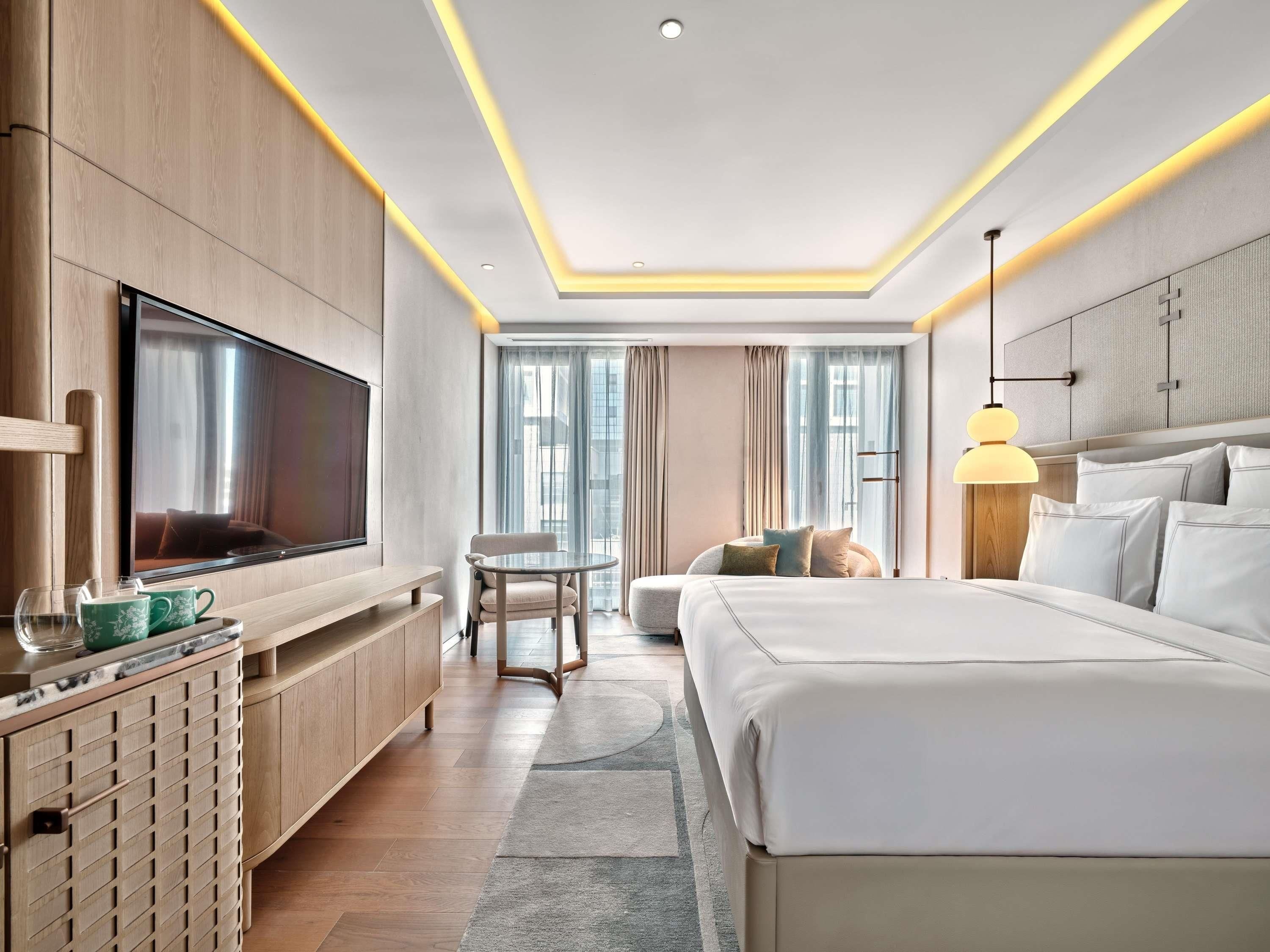 A modern hotel room with a large bed, a TV, a desk, and a sofa.