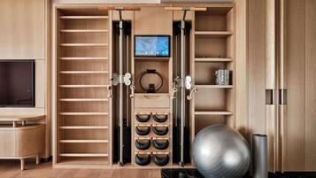 A room with a wooden wardrobe, a television, exercise equipment, and a black marble floor.