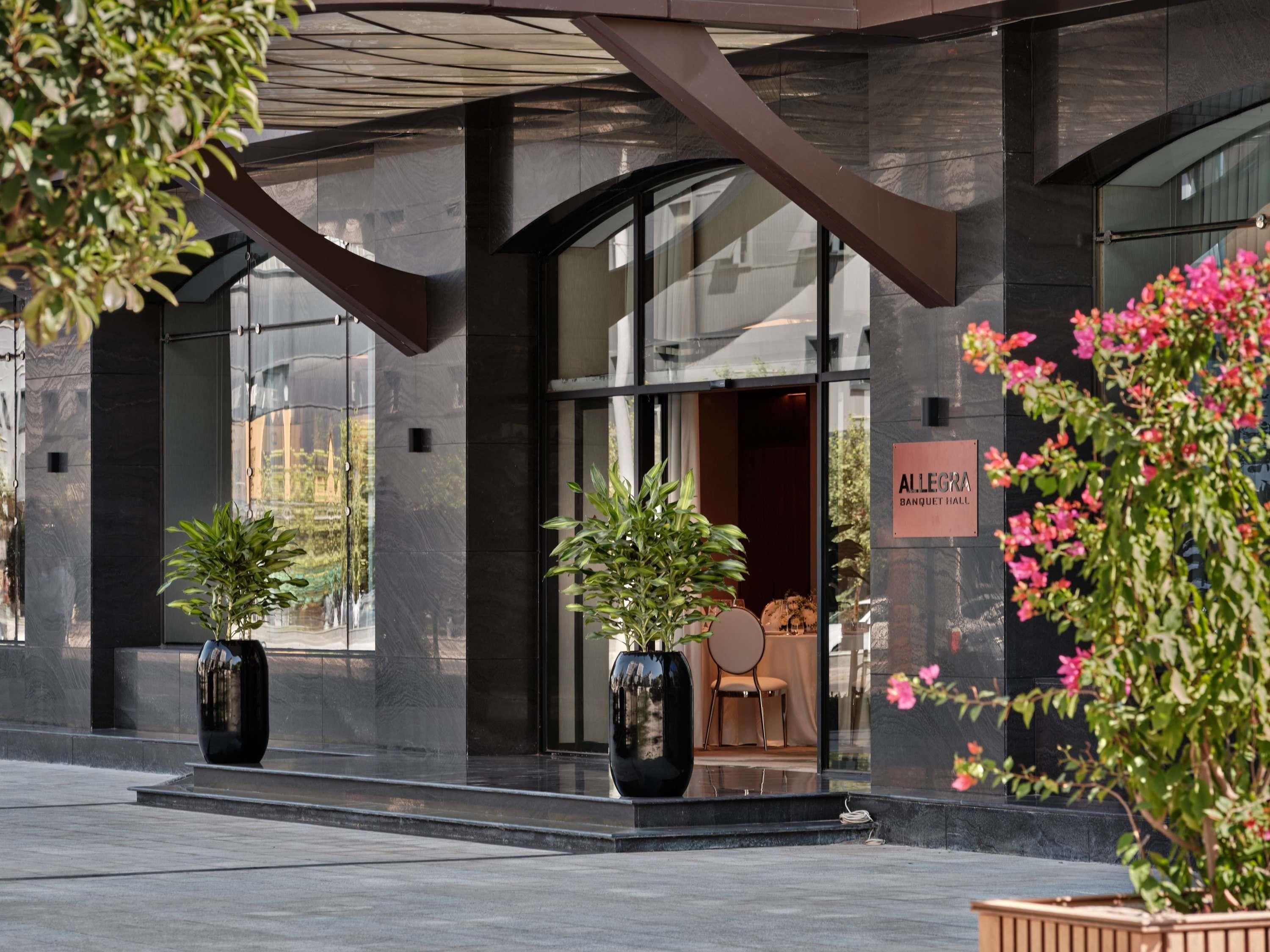 Un bâtiment moderne avec une entrée en verre, des plantes en pot et une enseigne indiquant un espace dédié aux banquets.