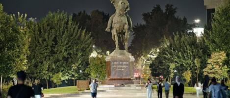 A statue of a historical figure on horseback, surrounded by a paved area with trees and people walking around.