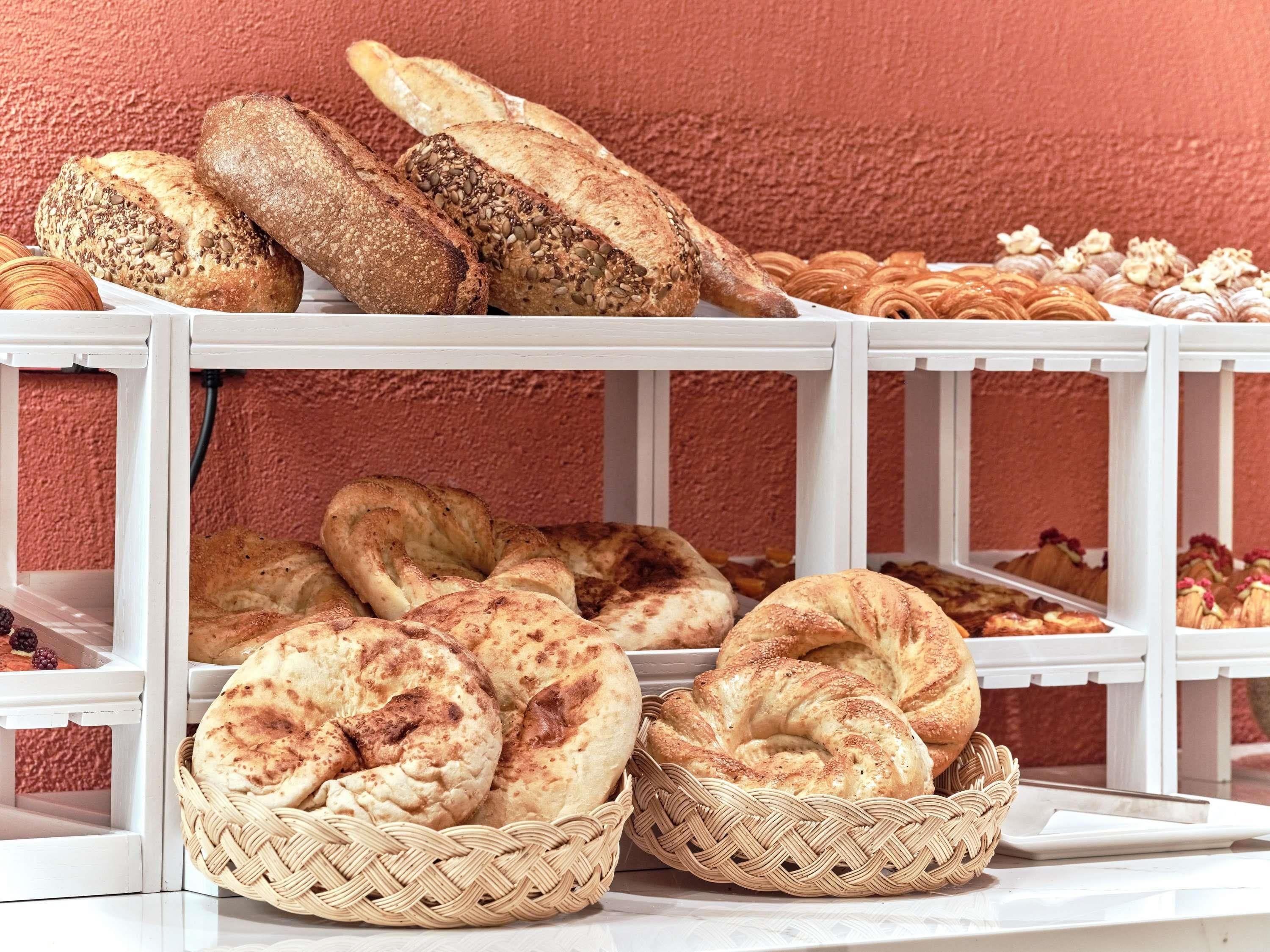 Una exhibición de panes y pasteles varios sobre un estante blanco frente a una pared con textura.
