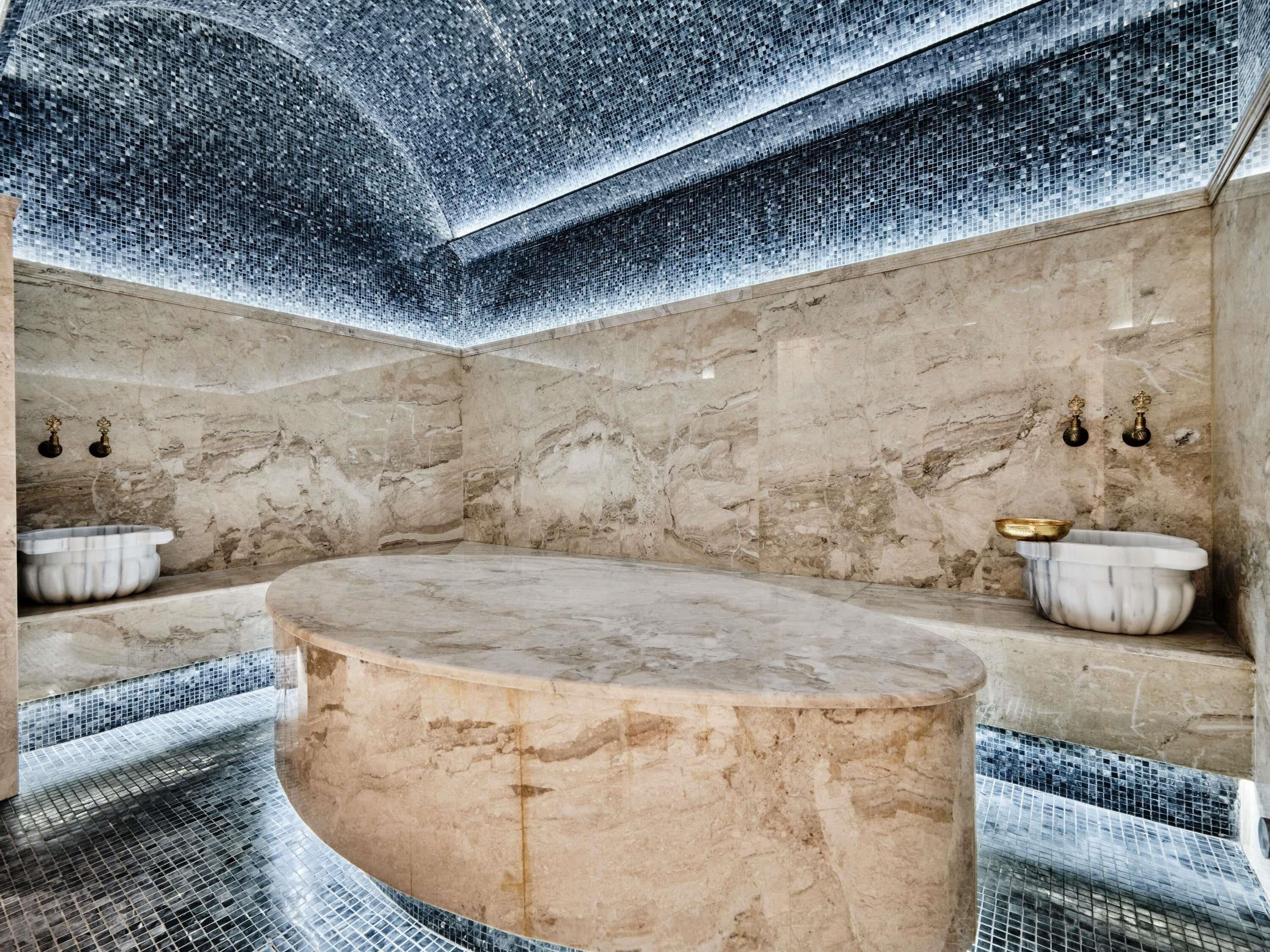 A marble bathroom with a freestanding bathtub, a small sink, and a wall-mounted basin.