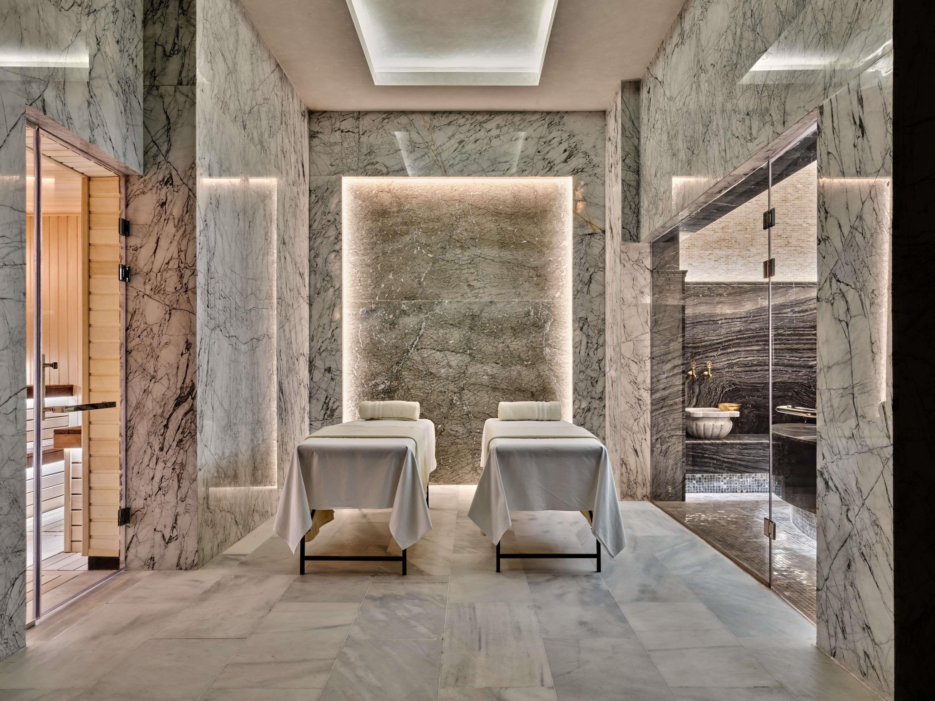 Een spa-ruimte met twee massagetafels, een stenen muur en uitzicht op een waterpartij.