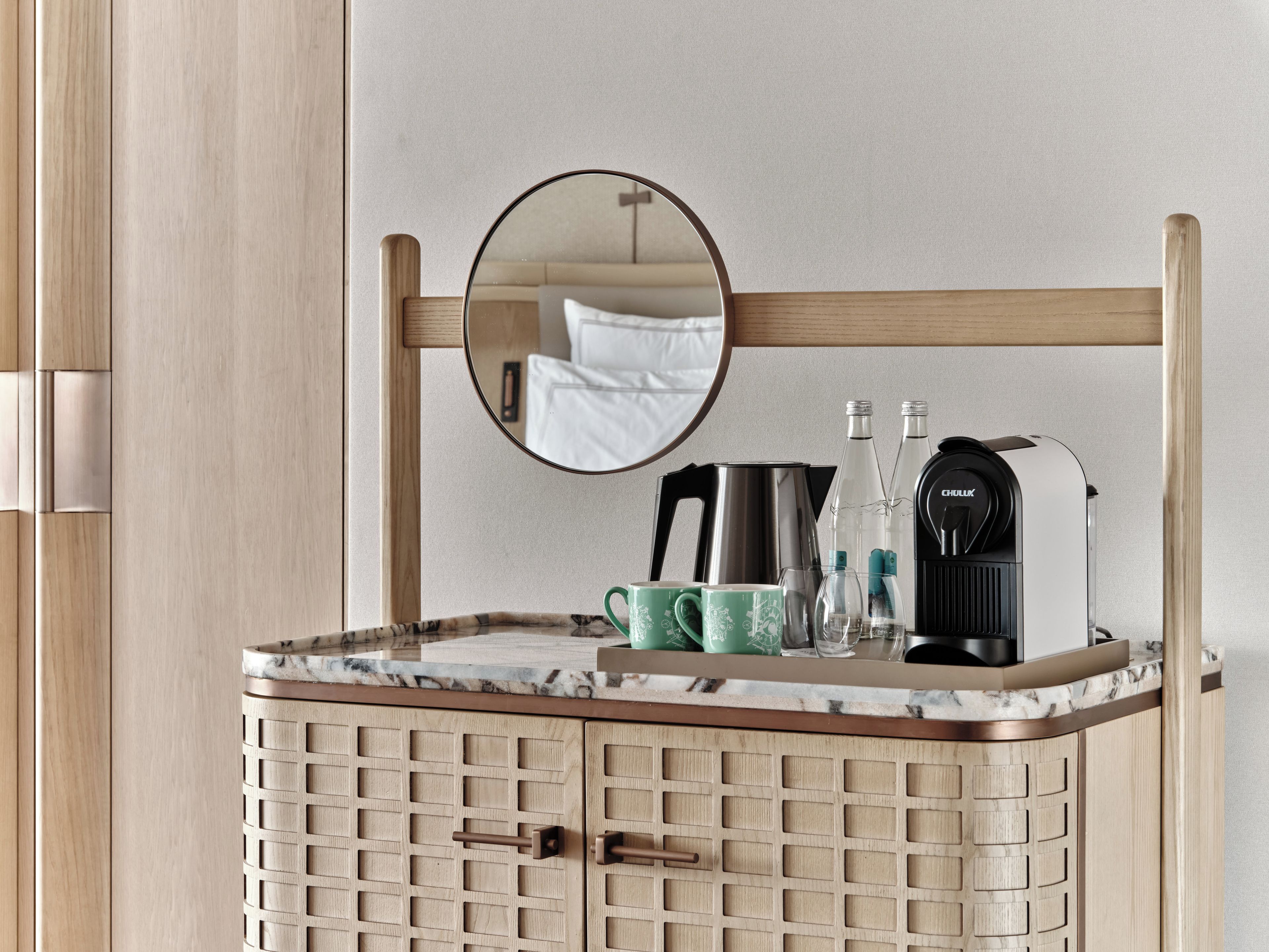 A bathroom with a wooden cabinet, a mirror, a coffee maker, and a kettle.